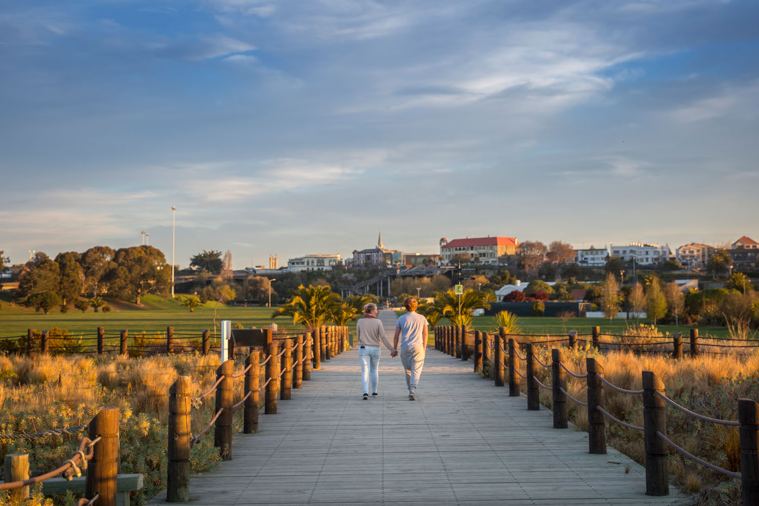 Couple holding hands walking through Caroline Bay towards city
